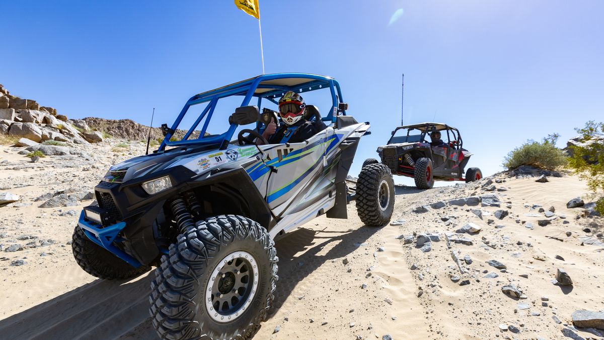 A driver and a passenger ride in a side-by-side across rocky desert ground at Desert Days.