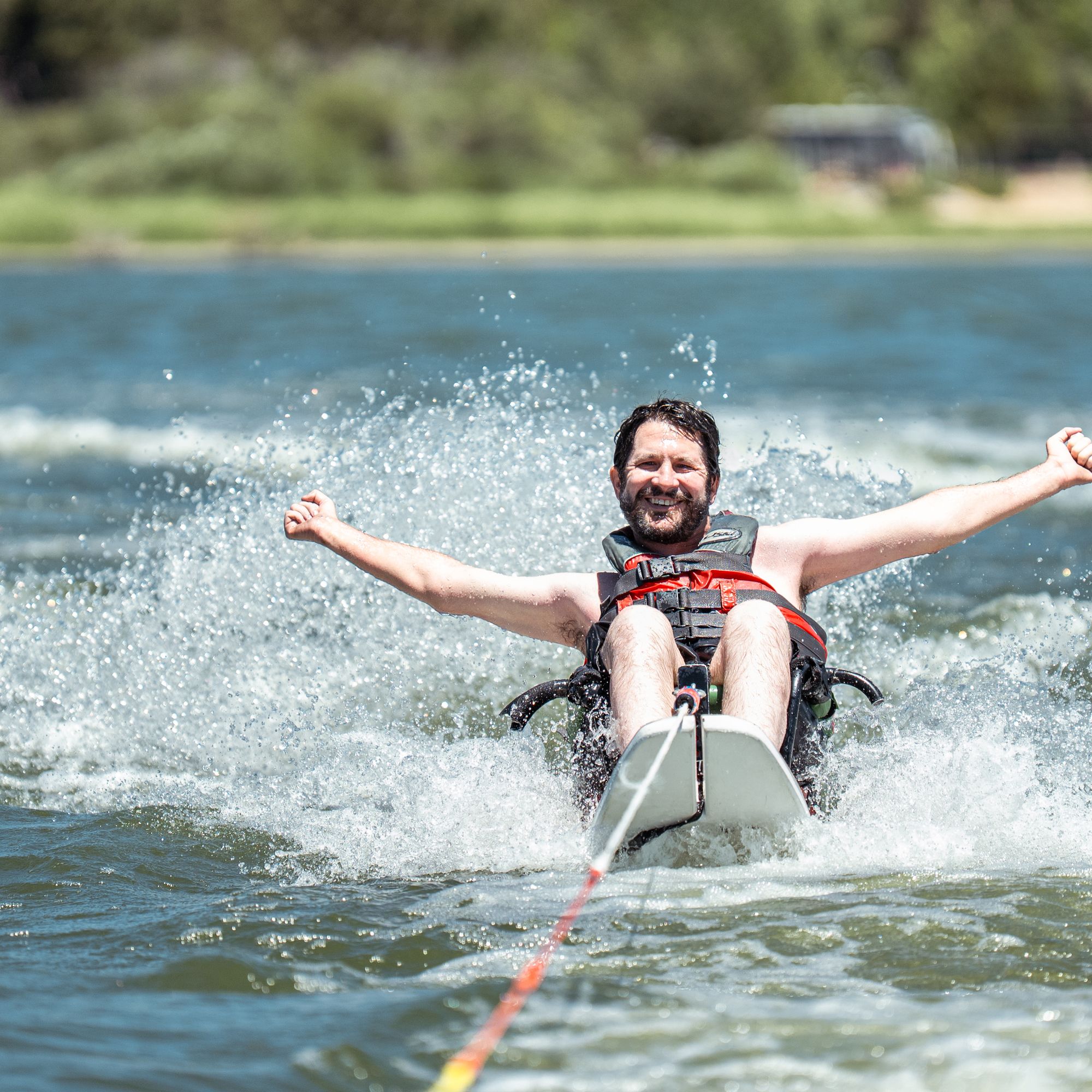 A participant on an adaptive sit-ski throws both arms wide and grins while being towed across Big Bear Lake.
