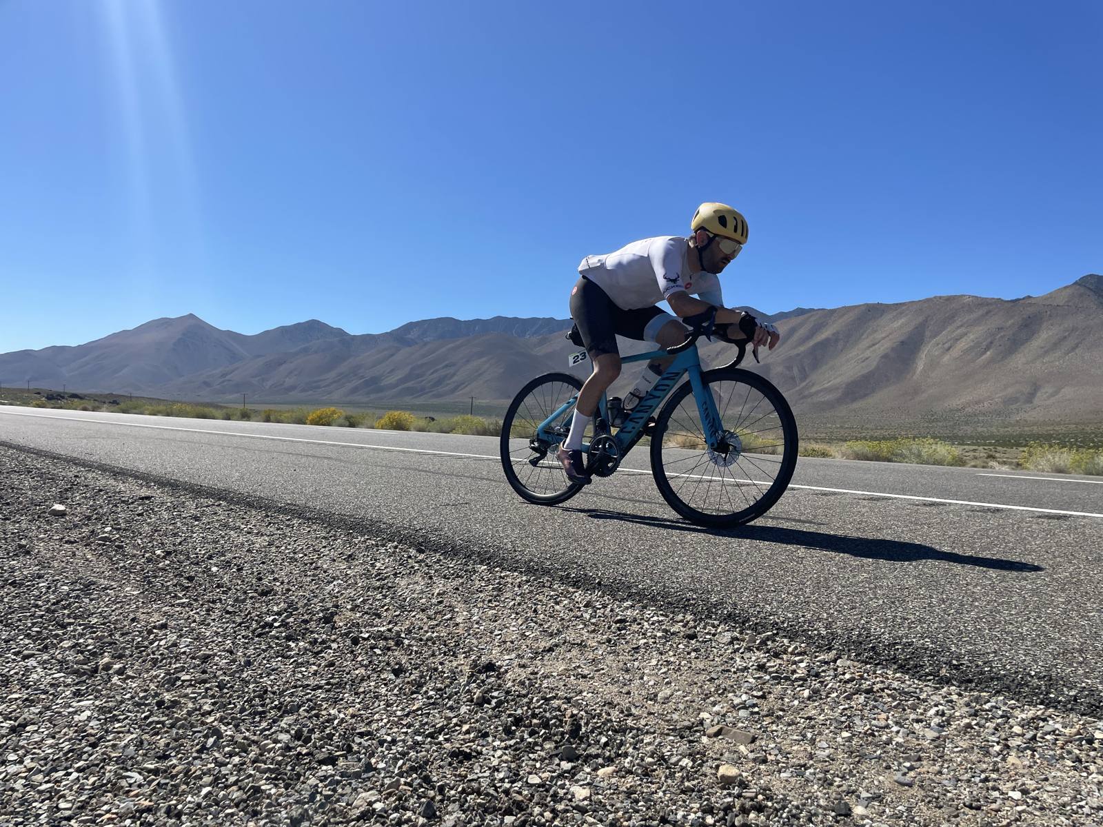 A Peak to Peak Pedal rider climbs the highway on a road bike, with desert mountains behind.