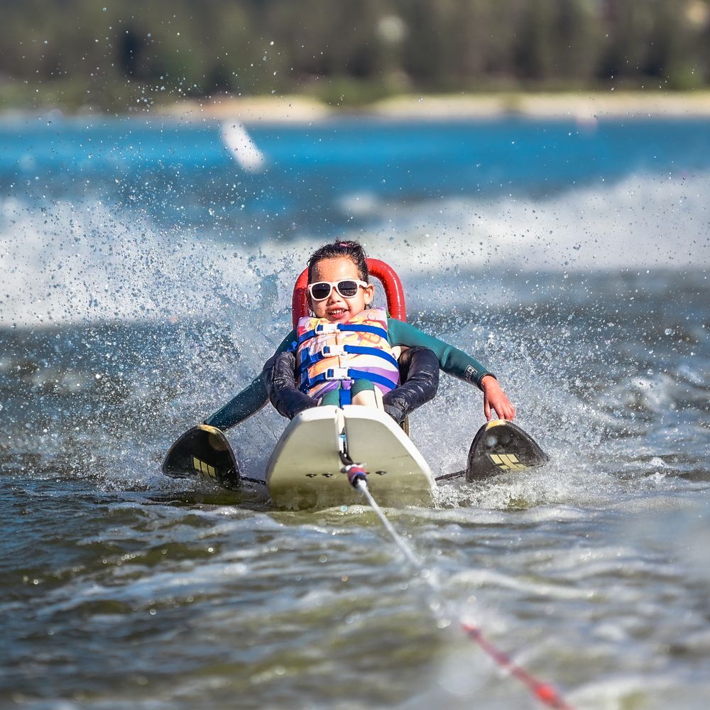 A young participant in sunglasses grins while water-skiing on an adaptive ski across Big Bear Lake.